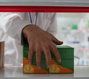 A pharmacist carefully places a box of pills on a shelf in a well-organized pharmacy setting.