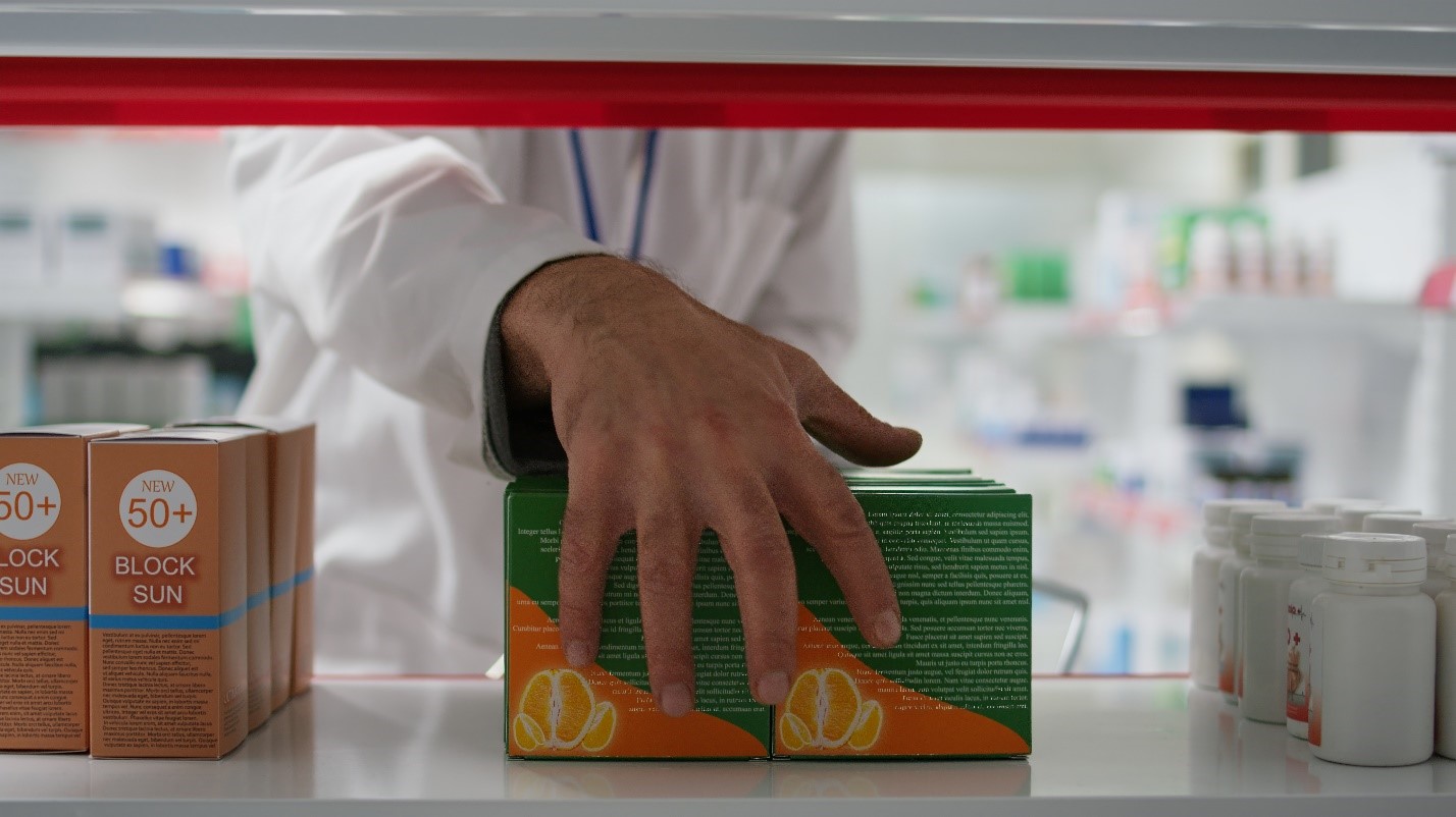 A pharmacist carefully places a box of pills on a shelf in a well-organized pharmacy setting.